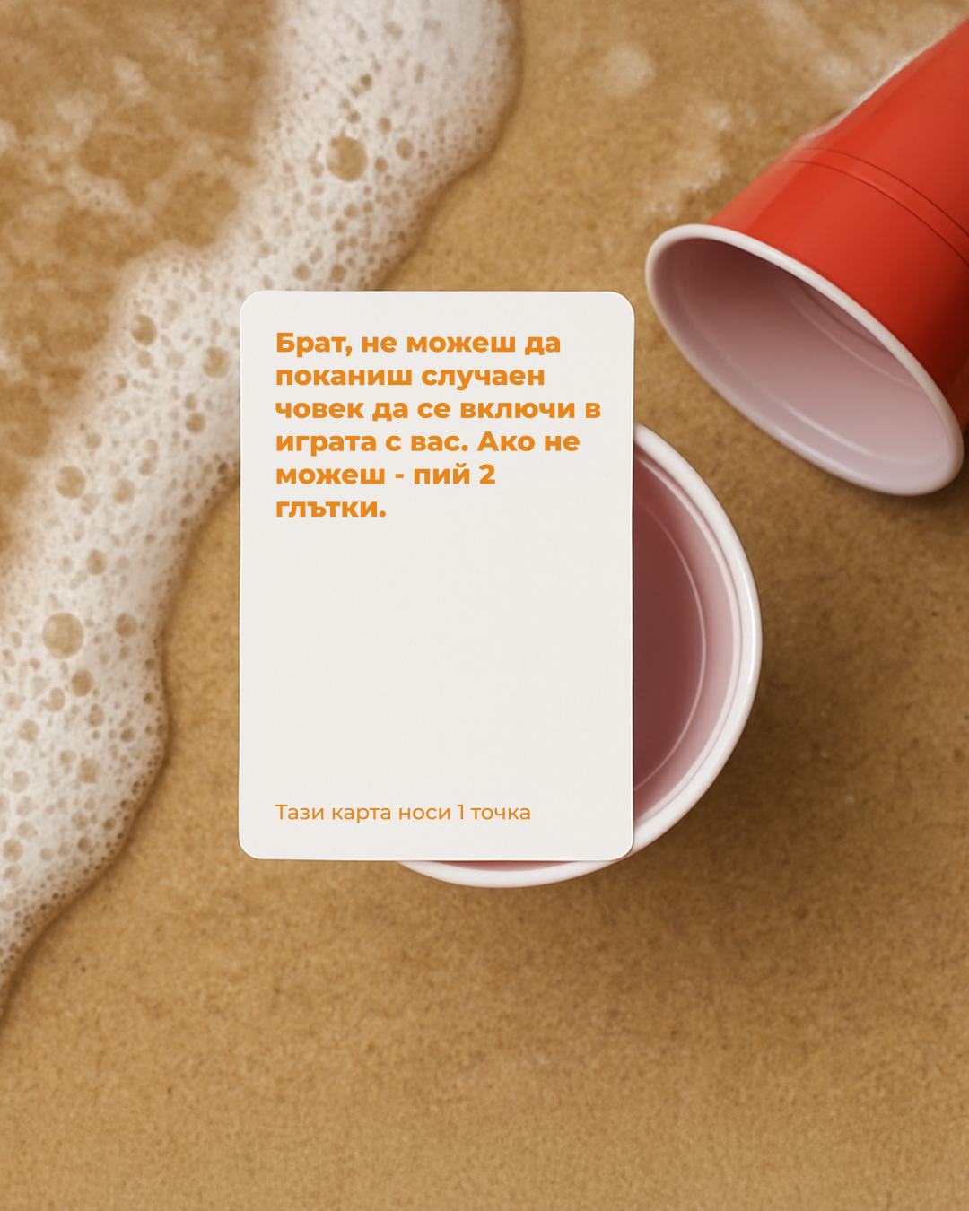 Карта от играта Брат, не можеш – Beach Edition, поставена върху червени парти чаши в пясъка до морска пяна.